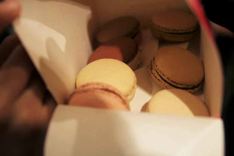 someone is holding a cardboard box with some macaroons in it
