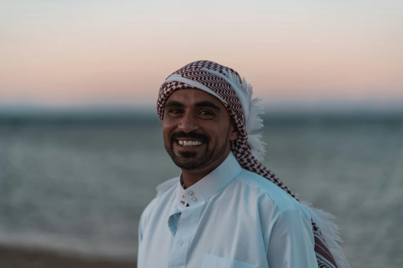 a middle eastern man in a turban stands on the beach
