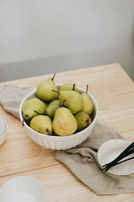 the bowl of pears is next to a plate of chopsticks