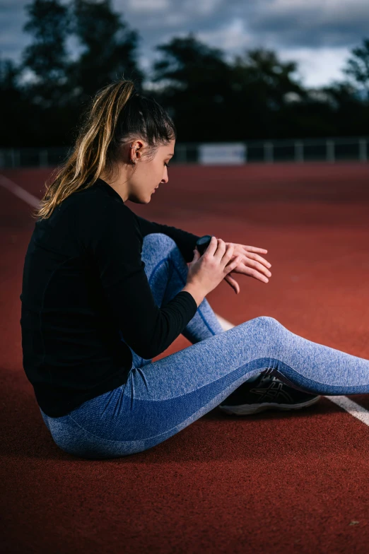 a woman wearing jeans is sitting down on a tennis court