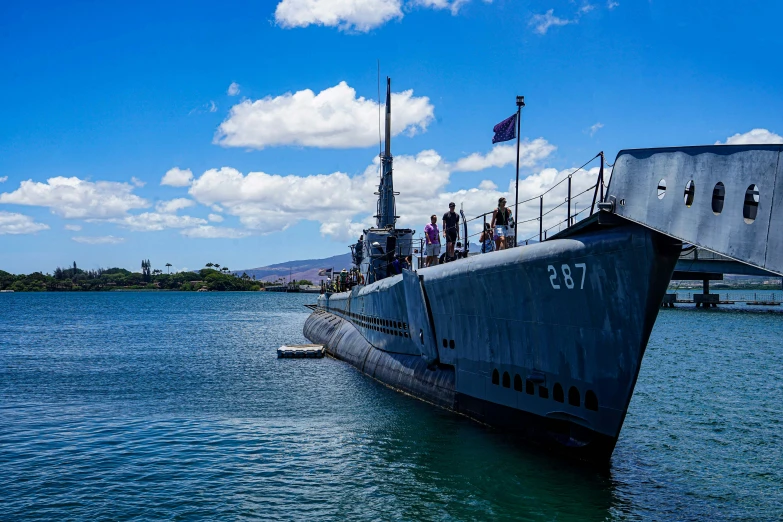 several people are aboard a navy submarine while another is on the deck