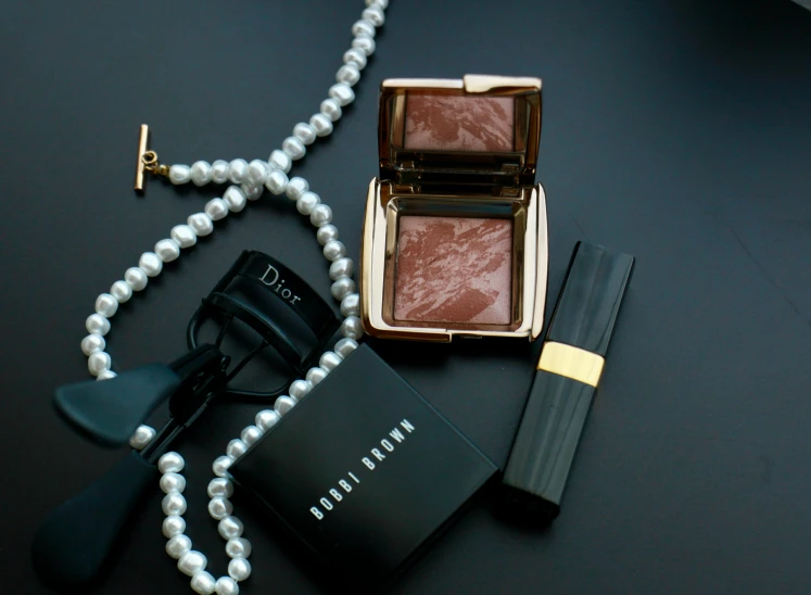 a pearl necklace and cosmetics are laying next to a pink powder