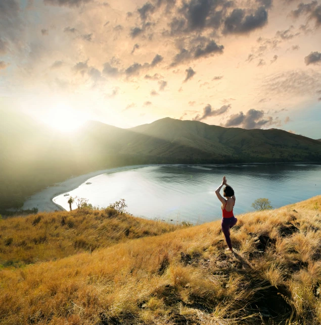 a girl standing on a cliff at sunset raising her arms in the air