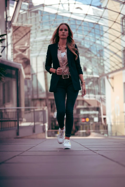 a woman in a suit and tennis shoes walks on a street