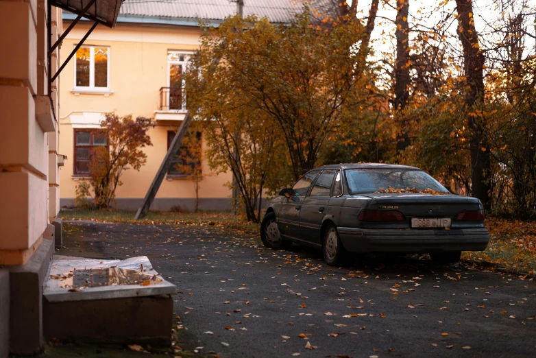 the car is parked beside of a tree and building