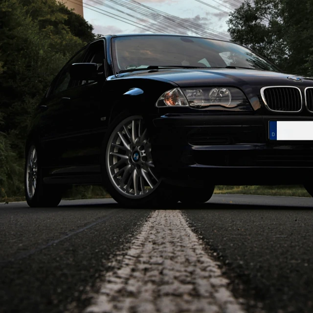 the front end of a black bmw parked on the side of a street