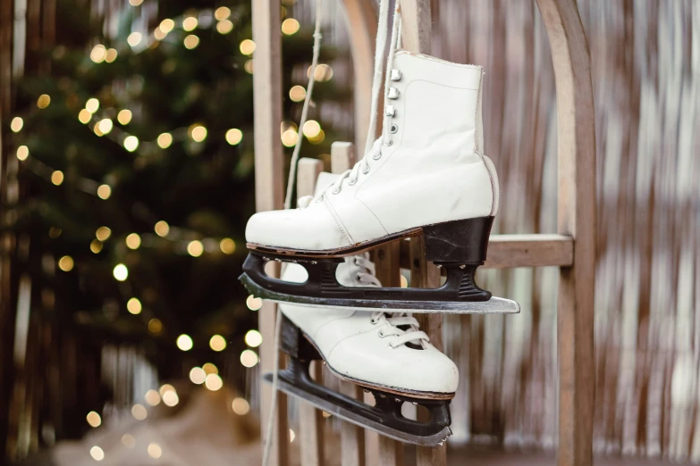 two ice skates sitting on a wooden slatted rail near a christmas tree