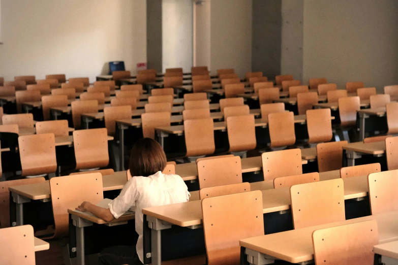 an empty room with many wooden chairs and a little girl sitting on the first row