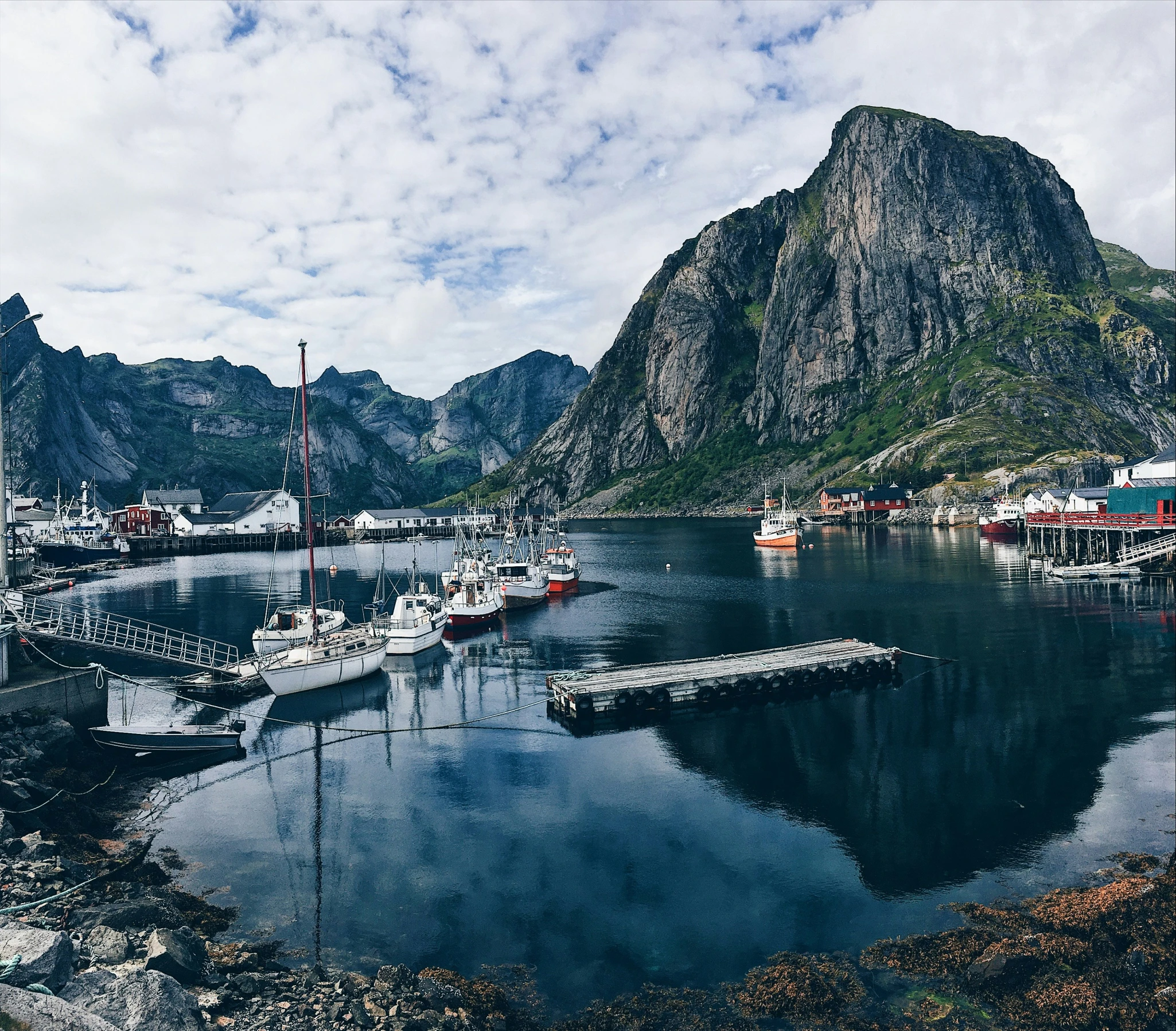 some small sailboats are docked and a mountain range is seen in the distance