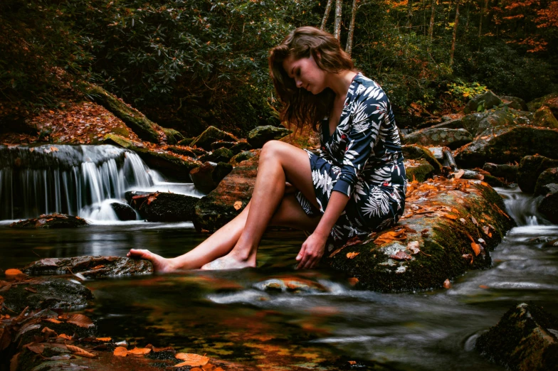 the woman is sitting on the rock next to the waterfall