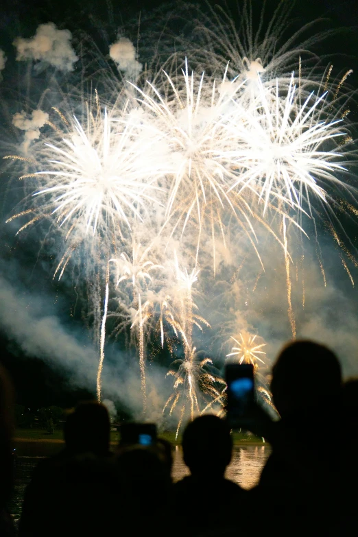 people are standing with their cell phones in front of fireworks