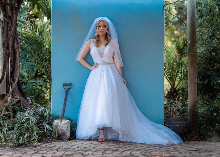 bride with veil leaning against wall in a white gown