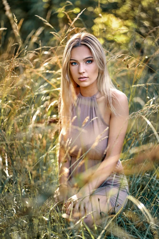 a woman posing in a grassy field with trees behind her