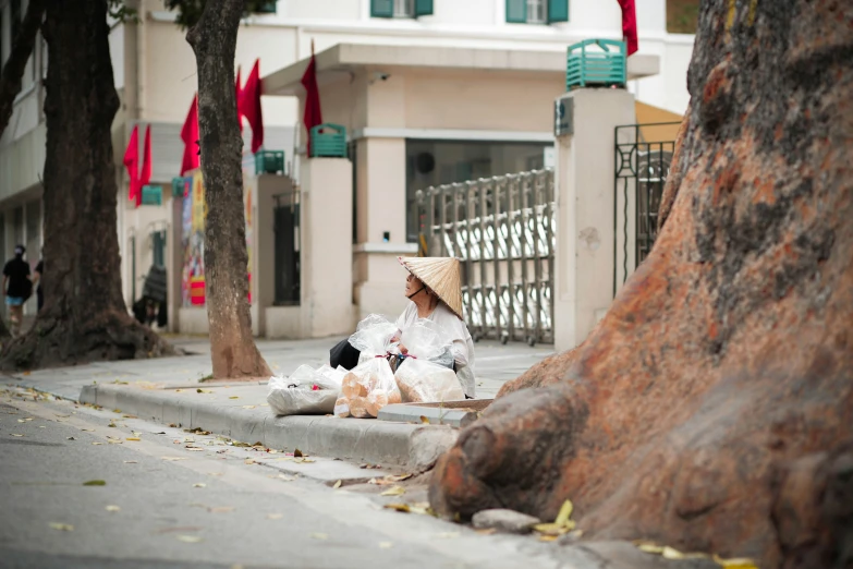 a woman is sitting on a street corner wearing a straw hat