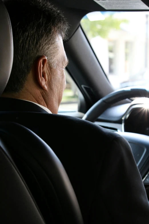 man in suit and tie driving a car with his head turned back