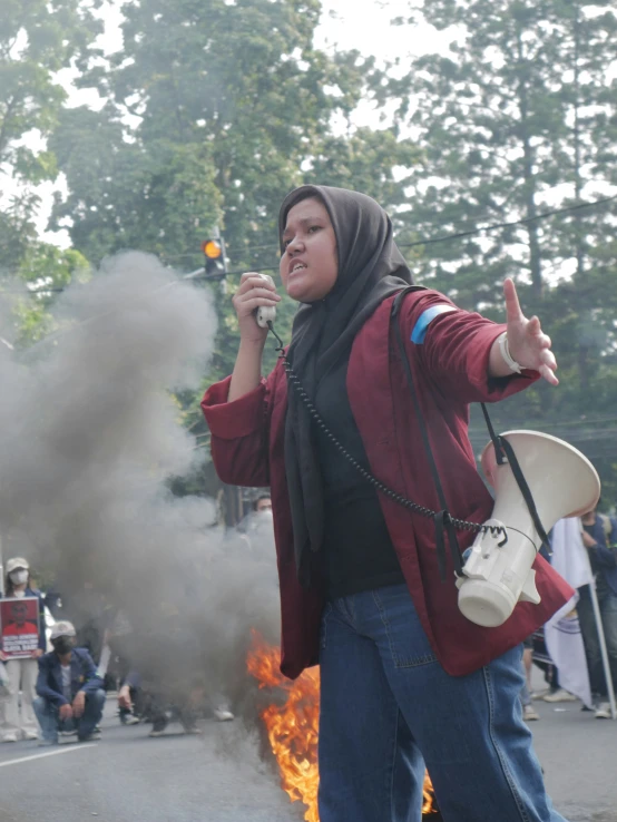 a woman with a phone standing in front of a fire and holding soing