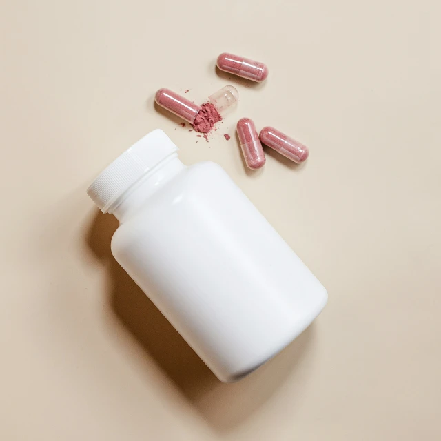 several pink pills and a white pill bottle on a surface
