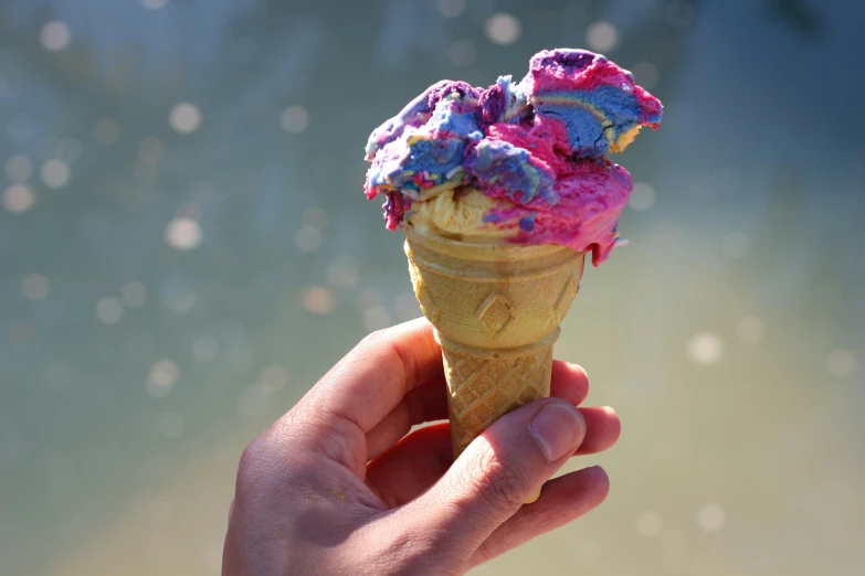 a hand holding an ice cream cone with rainbow sprinkles