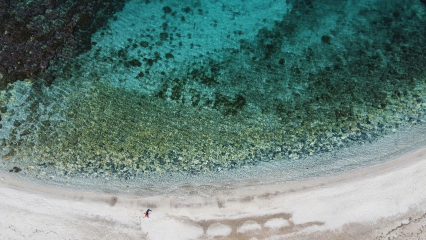 an aerial view of the ocean and beach with the person walking in the water