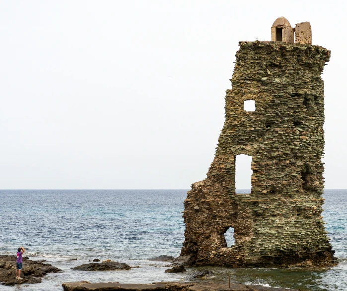 two people walking along the ocean past an old lighthouse