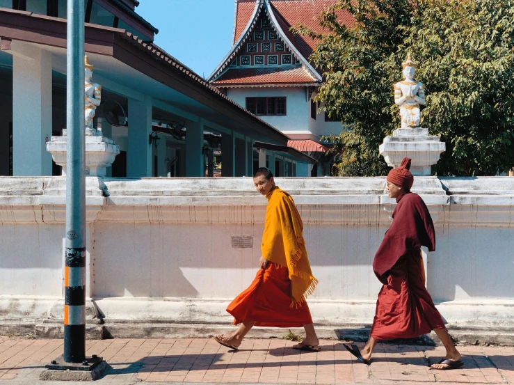 two men in orange and yellow outfits walking in front of a white building