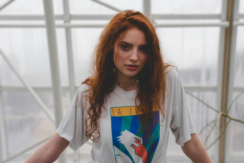 young woman with long red hair and makeup looking to the side in a greenhouse