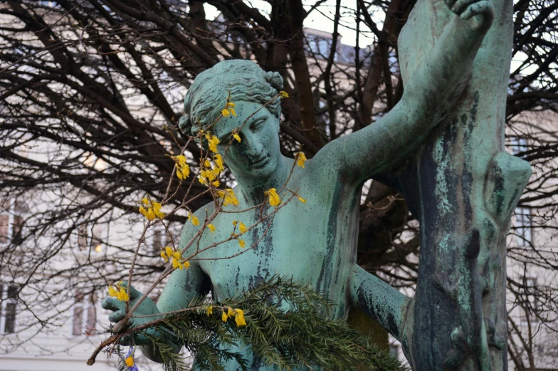 a statue in the foreground, with yellow flowers in its arm and nches in the background