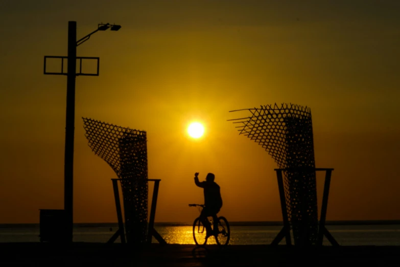 the silhouette of a person on a bicycle riding toward the setting sun