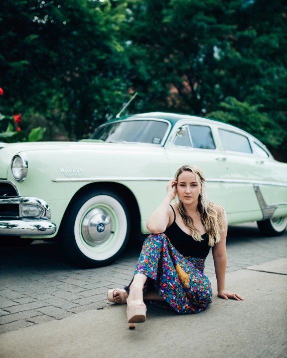 a woman sitting on the sidewalk in front of a car