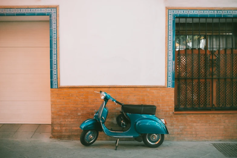 an old scooter sits in front of a brick wall and doorway