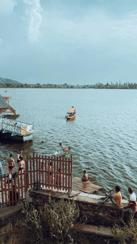 people sitting by the lake watching boats pass