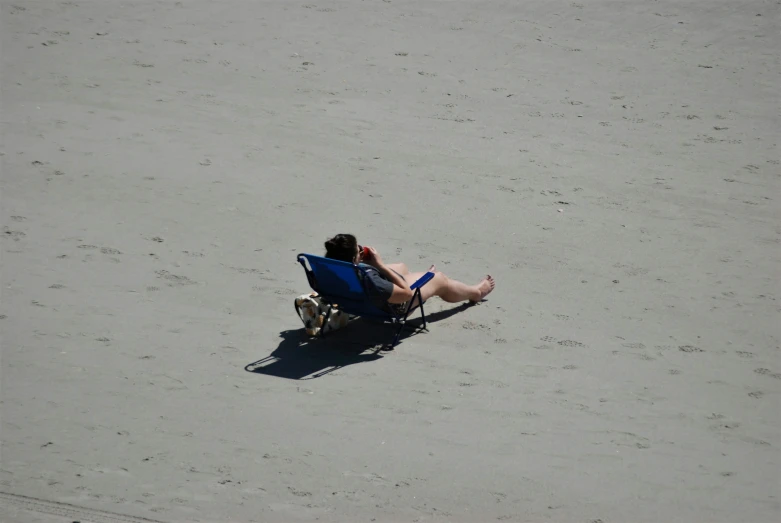 a man lying in a blue lawn chair on the beach