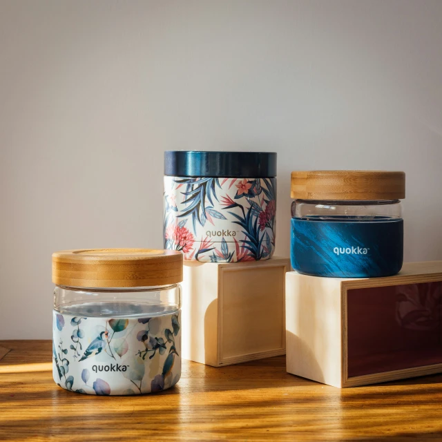 four jars with flowers are displayed on a wooden table