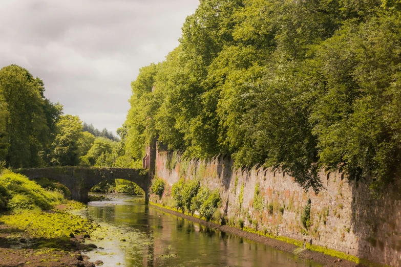 a river next to a stone wall and green grass