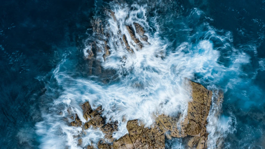 aerial view of the blue ocean with waves crashing to the rocky shore