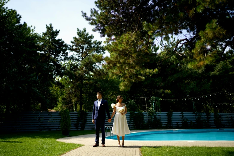 a man and woman standing on the pathway near a pool