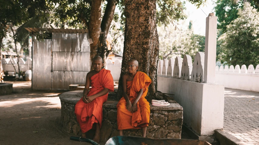 two monks sitting under trees outside on concrete slabs