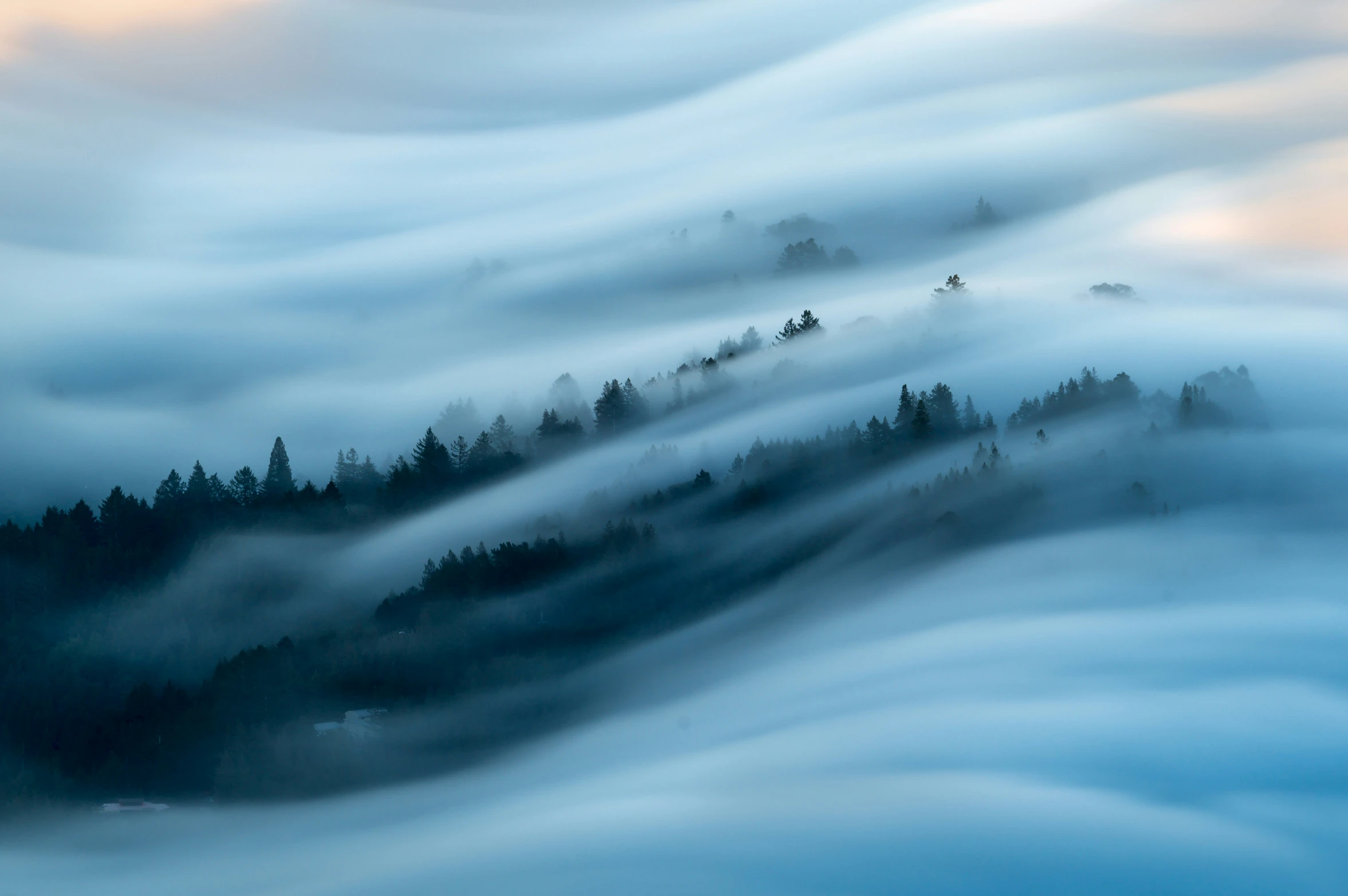 fog rolling in to a mountain with a house on the top