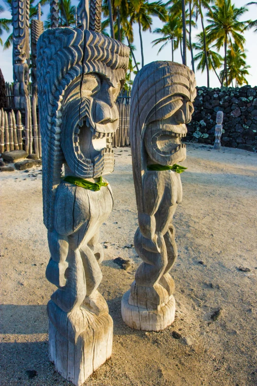 two stone statues on the sand with palm trees
