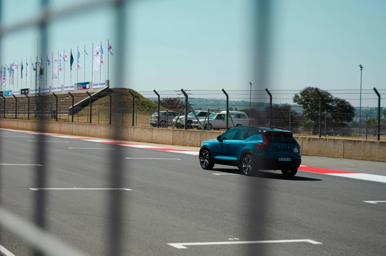 a small blue car traveling down the road in a fenced parking lot