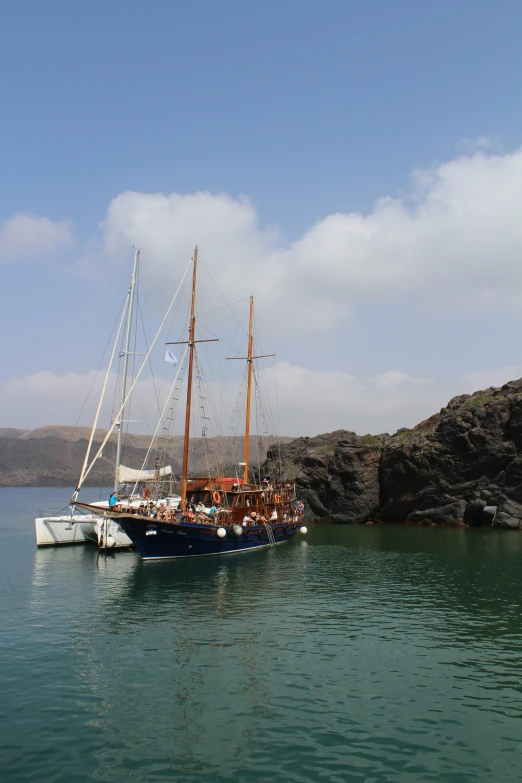 boats with sails anchored in water near rocky shore