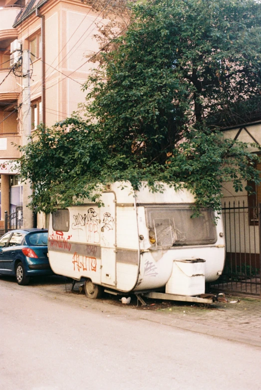 a white trailer with graffiti parked in front of a tree