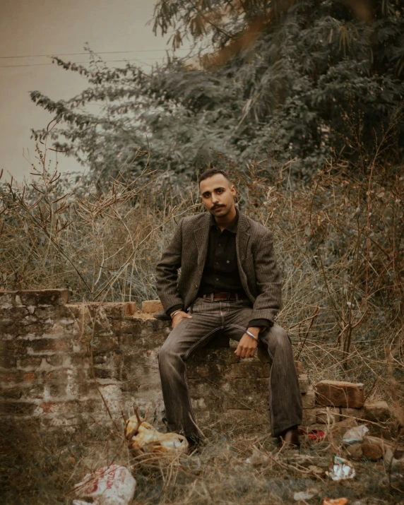 man sitting on concrete structure next to weeds and trees
