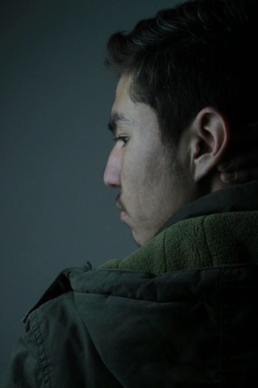 a young man in a dark room wearing a jacket