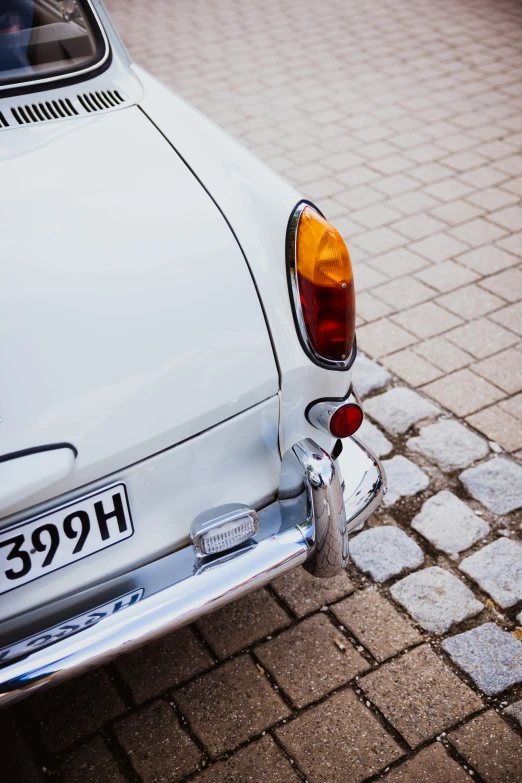 a white car with a number plate on it parked on some cobblestone