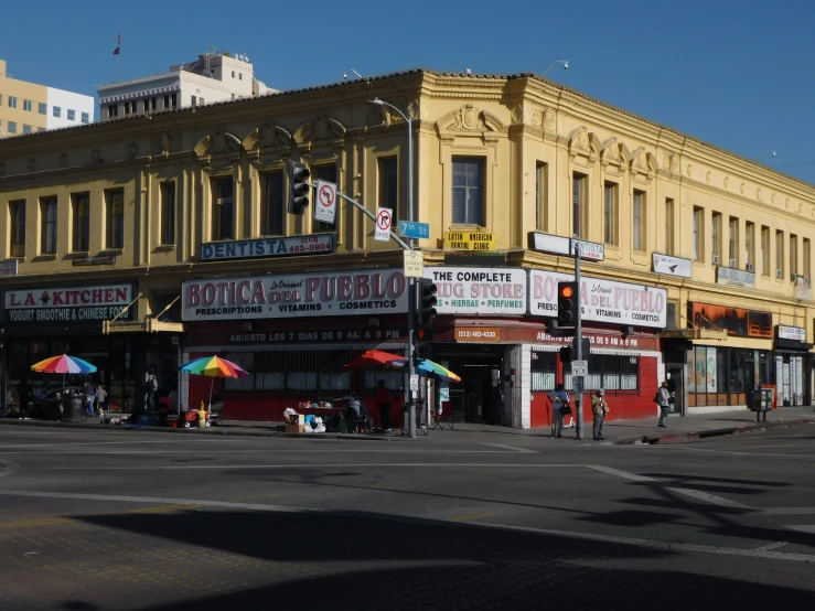 some people are walking on the sidewalk in front of a yellow building