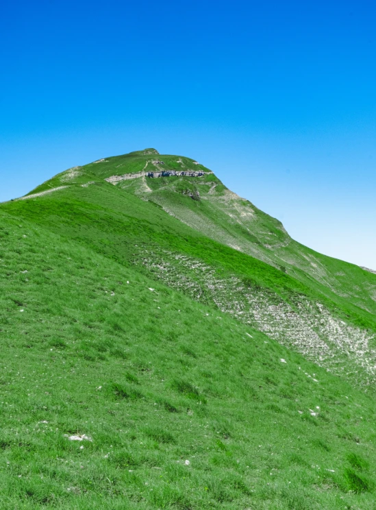 there is a green grassy hill on the side of the mountain