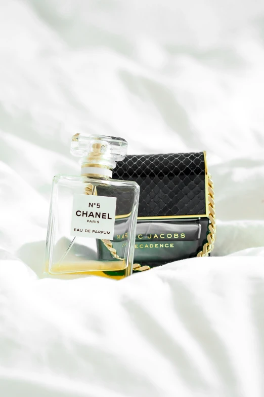 perfume bottle sitting on white sheet next to handbag