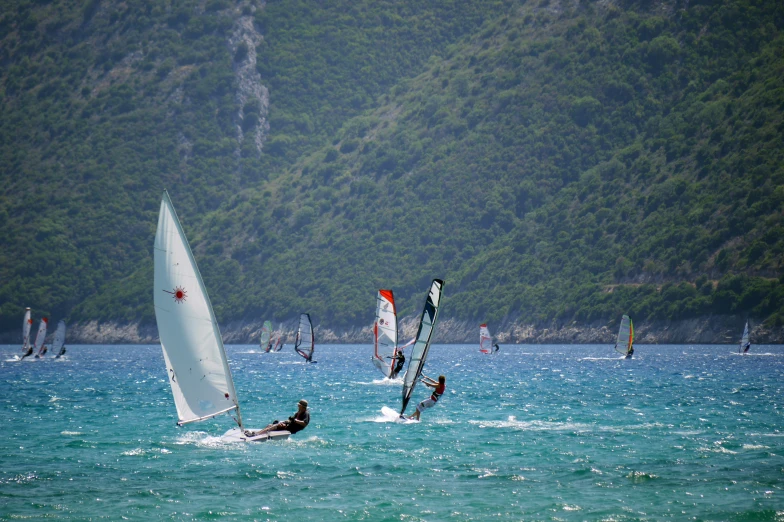 several wind surfiers in the ocean near a cliff