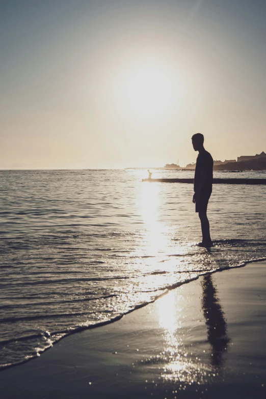 the man is standing near the beach as the sun sets